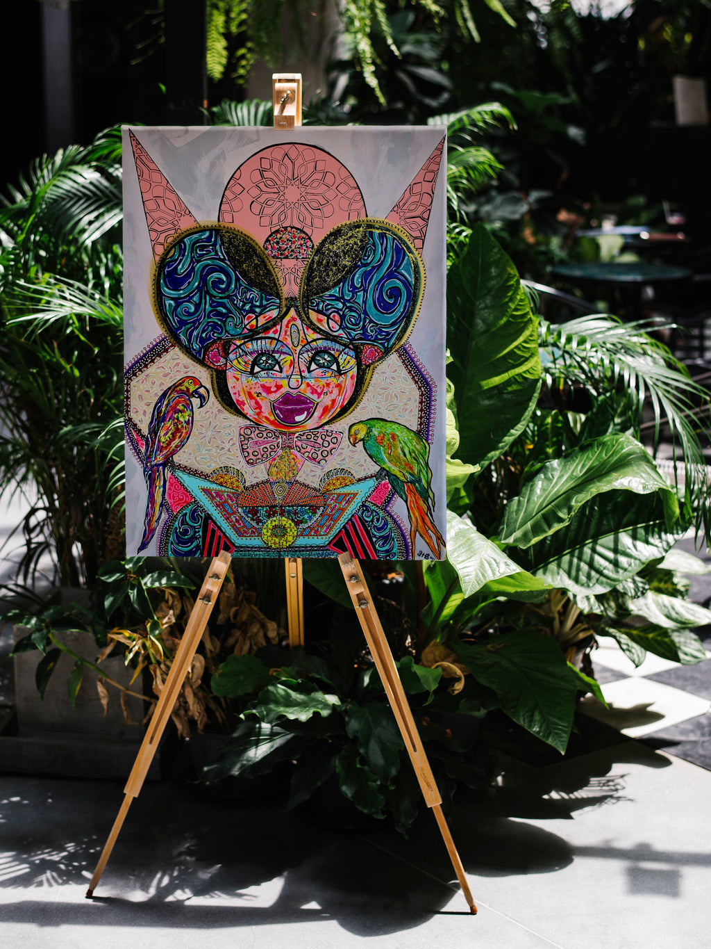 Kitty Kat propped on a wooden easel outdoors among tropical palms and ferns