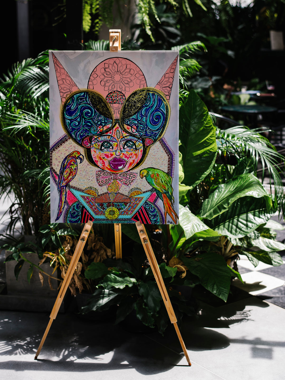 Kitty Kat propped on a wooden easel outdoors among tropical palms and ferns